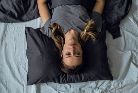 Young sad woman lying on a bed with eyes opened